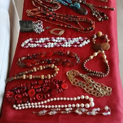 Collection of vintage fashion jewelry laid out on a red surface, featuring beaded necklaces, chunky statement pieces, gold-tone chain...