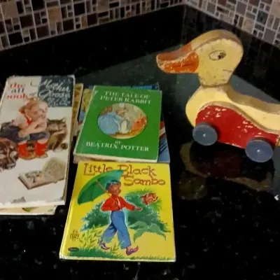 Vintage children's books, including The Tale of Peter Rabbit and Little Black Sambo, alongside a worn wooden duck pull toy with wheels.
