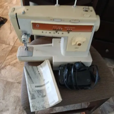 Vintage Singer Stylist electric sewing machine, featuring an off-white body with brown accents, complete with foot pedal, power cord, and...