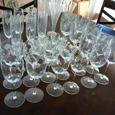 Large collection of crystal and glass stemware, including wine goblets, champagne flutes, and cocktail glasses arranged on a dark wooden...