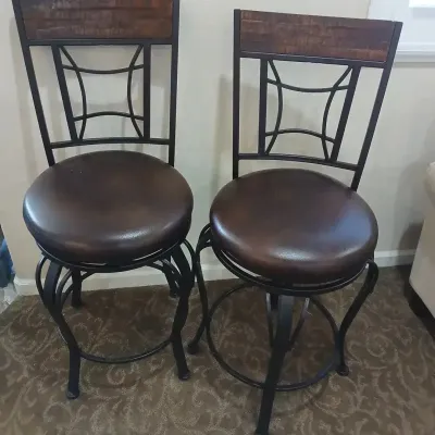 Pair of contemporary metal swivel barstools featuring dark brown faux-leather cushioned seats and wood-accented backrests.