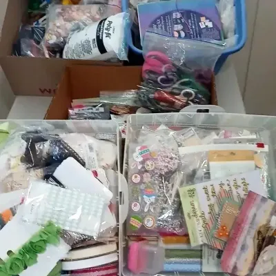 Assorted crafting supplies, ribbons, stickers, and sewing notions organized in plastic bins and cardboard boxes.