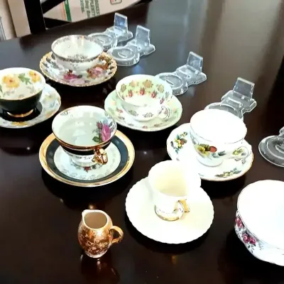 Assorted vintage porcelain teacups and saucers with floral motifs and gilt accents, arranged alongside display stands and a small creamer...