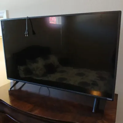 Vizio flat-screen television with original stand legs, shown resting on a wooden surface with power cord draped over the top frame.