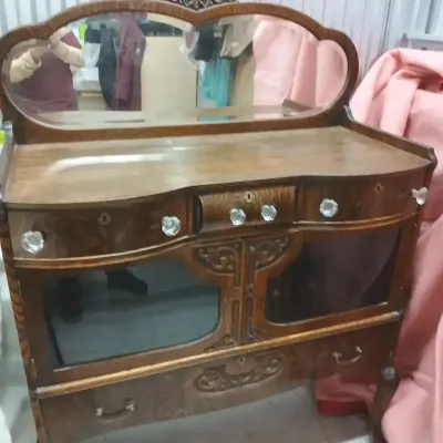 Antique oak curved-glass china cabinet server with an attached shaped top mirror, glass knobs, and carved wood accents.