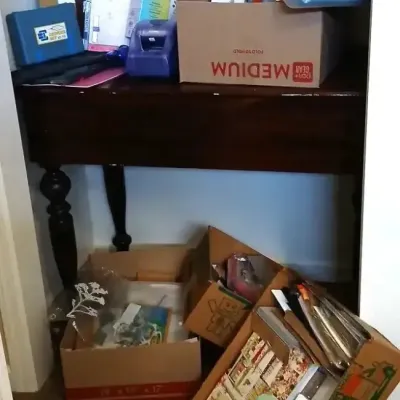 Dark wood console table with turned legs, stacked with office supplies, label makers, paper, and boxes of crafting materials.