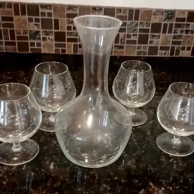 Five-piece etched clear glass decanter set, featuring a bulbous decanter with a flared neck and four matching brandy snifters with floral...