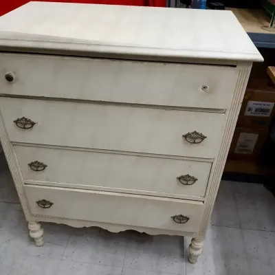 Off-white painted four-drawer dresser with ornate bronze-tone hardware, fluted side details, and turned legs.