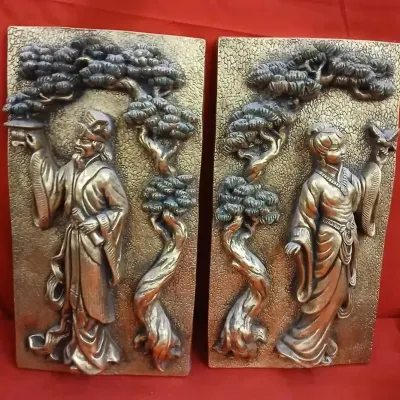 Pair of vintage Chinoiserie-style metallic cast wall plaques depicting a man and woman in traditional attire under pine trees.