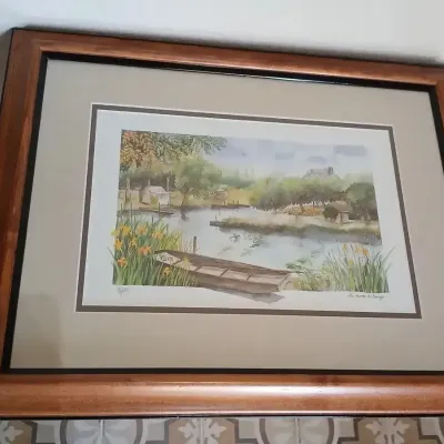Framed watercolor print depicting a serene river scene with a wooden boat, double-matted in a finished wooden frame.