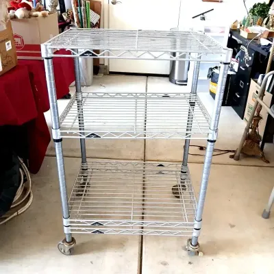 Three-tier Metro chrome wire rolling utility cart with caster wheels.