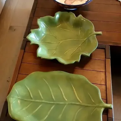 Pair of green glazed ceramic leaf-shaped serving platters, displayed alongside a hand-painted ceramic bowl with a moose motif.