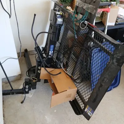Motorized hitch-mounted mobility scooter or wheelchair carrier lift with folding wire mesh platform.