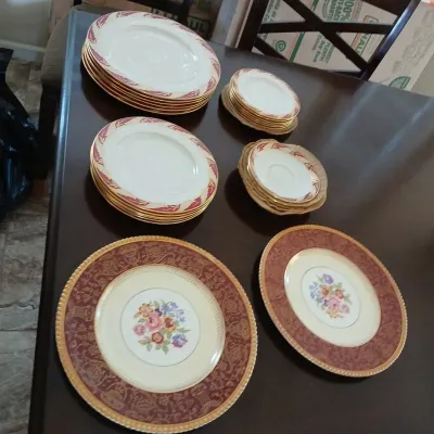 Collection of vintage porcelain china plates featuring gold rims, floral centers, and burgundy leaf trim patterns.