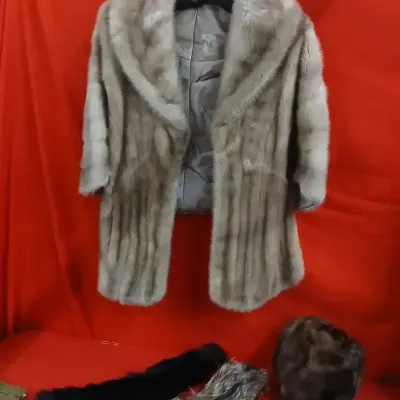 Vintage light brown mink fur coat shown hanging alongside a fur hat and fur collars.