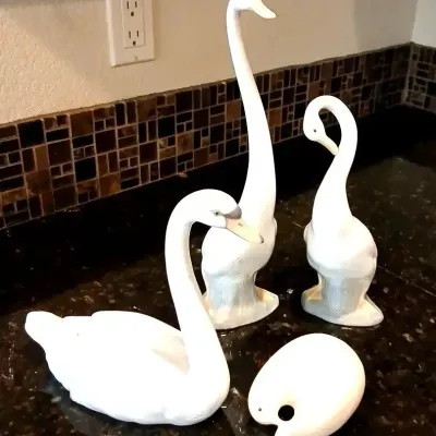 Set of four vintage white ceramic swan figurines in various graceful poses displayed on a countertop.