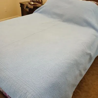 Light blue quilted bedspread with intricate medallion and border stitching pattern.