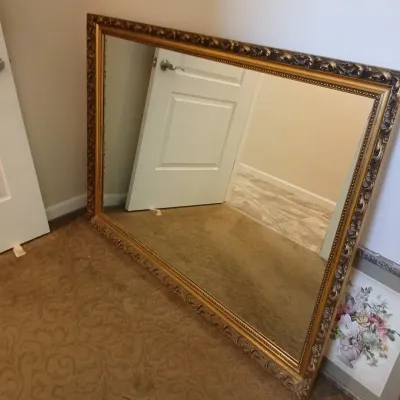 Large rectangular wall mirror in an ornate gilt and dark-toned moulded frame, resting on the floor.