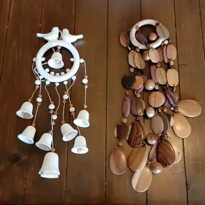 Pair of decorative hanging wind chimes, including a white ceramic bell chime featuring lovebirds and a natural wood slice chime.