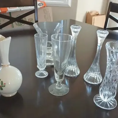 Collection of assorted glassware including clear cut-glass vases, candlestick holders, stemware, and a small ceramic holly-motif bud vase.