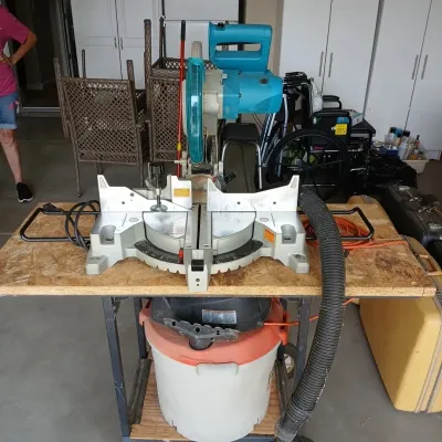 Makita compound miter saw mounted on a portable workbench with a shop vacuum connected below.