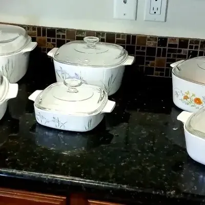 Collection of vintage CorningWare casserole dishes with glass lids, featuring floral and plant motifs including Shadow Iris and Country...