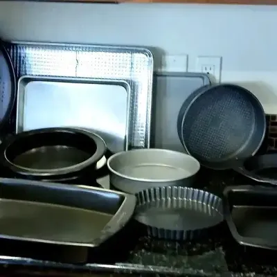 Assortment of modern baking cookware, including sheet pans, cake tins, pie plates, a muffin tin, and a tart pan on a kitchen countertop.