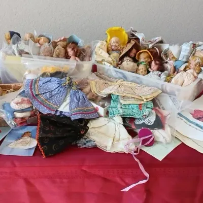 Large collection of vintage small dolls, doll clothes, and accessories displayed on a red tablecloth.
