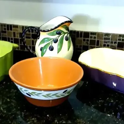Collection of colorful kitchen ceramics, featuring a lime green covered Dutch oven, olive-themed pitcher and mixing bowl, and a purple...