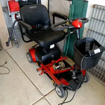 Pride Mobility red and black four-wheel mobility scooter equipped with a front basket, vinyl padded seat, and an attached Novara trailer...