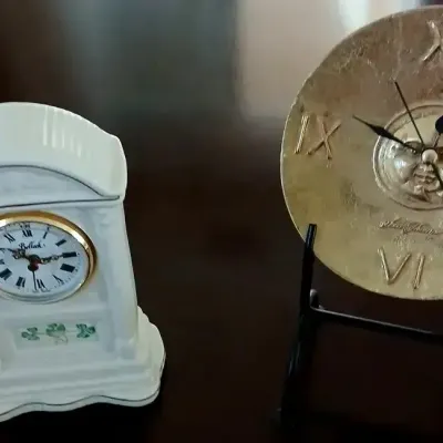 Pair of decorative clocks, including a white Belleek porcelain mantle clock with shamrock details and a metallic round desk clock...