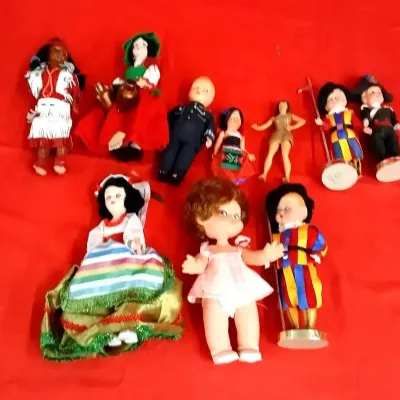 Collection of vintage miniature souvenir and novelty dolls in cultural and character attire, laid out on a red fabric surface.