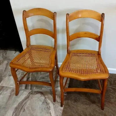 Pair of vintage ladderback dining chairs with woven cane seats and warm wood finish.
