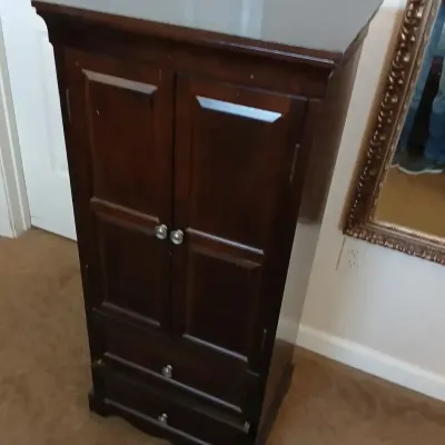 Traditional dark wood jewelry armoire featuring two panel doors over two lower drawers with silver-tone hardware.
