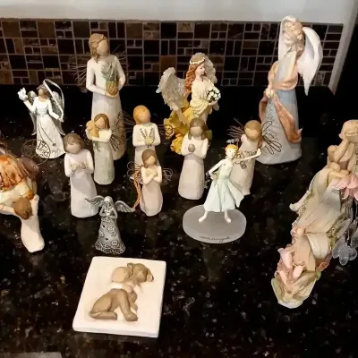 Large collection of decorative angel figurines, including several Willow Tree resin statues, displayed on a dark countertop.