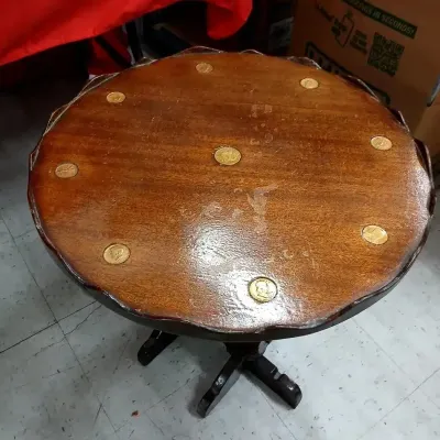 Round wooden accent table featuring inlaid coins around the scalloped tabletop, showing surface wear and finish distress.