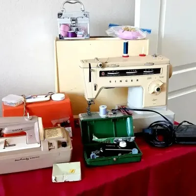 Collection of vintage sewing equipment, featuring a Singer Stylist machine, a beige Singer Sewhandy electric child's machine, and a...