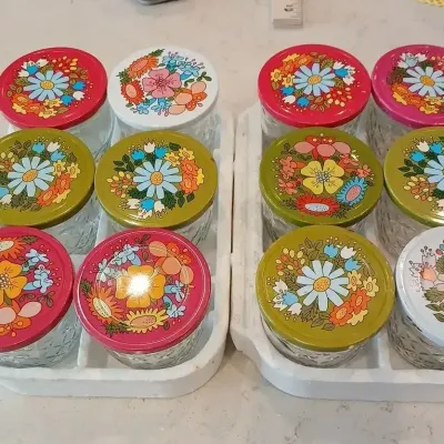 Set of 12 vintage Ball glass jelly jars featuring colorful 1970s floral painted metal lids.
