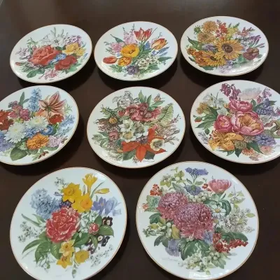 Set of eight vintage decorative porcelain collector plates featuring colorful floral bouquet illustrations with gilt trim.