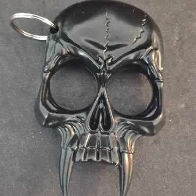 Sale Photo Thumbnail #43: Black skull-shaped self-defense keychain tool featuring prominent fangs and two finger openings.