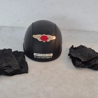 Sale Photo Thumbnail #54: Matte black half-shell motorcycle helmet featuring a Harley-Davidson sticker, shown alongside two pairs of worn black fingerless leather riding gloves.