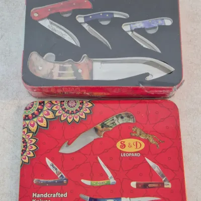 Sale Photo Thumbnail #45: S&D Leopard handcrafted knife collection in a decorative red metal collector's tin, featuring four folding pocketknives and one fixed-blade hunting knife.
