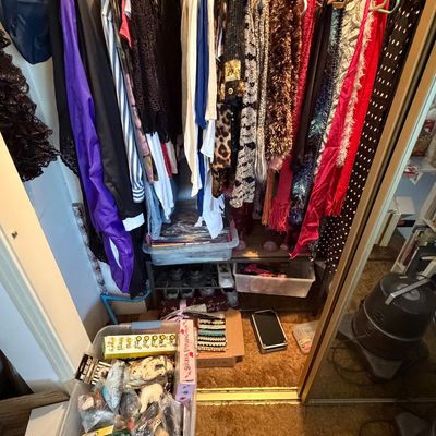 Closet packed with women's vintage and modern clothing, including tops, dresses, scarves, and accessories alongside storage totes...
