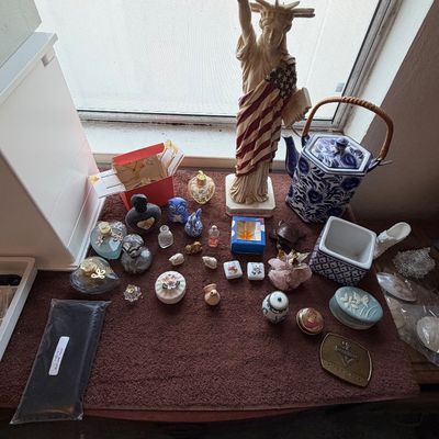 A table displayed with various collectibles, including a Statue of Liberty figurine wrapped in an American flag, perfume bottles, small...