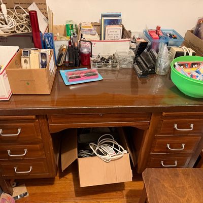 Vintage wood executive desk filled with assorted office supplies, stationery, cables, and small household items.