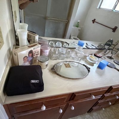 Assorted bathroom accessories on a counter, including a Wahl hair clipper kit, vintage glass canisters, hand mirrors, and decorative trays.