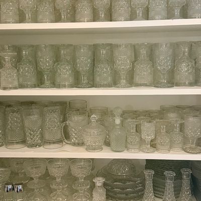 Large collection of vintage crystal glass stemware, tumblers, decanters, and serving pieces displayed on shelving.