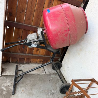 Portable electric cement mixer with red drum mounted on a wheeled black steel frame, showing light wear.