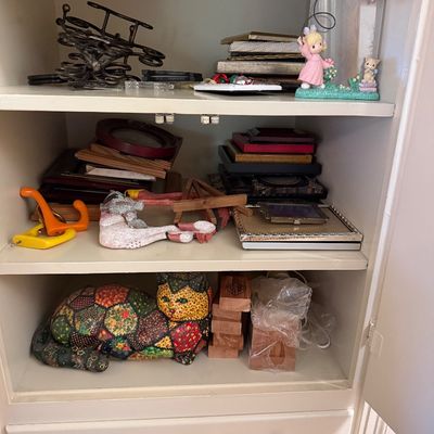 Cabinet shelves filled with home decor items including picture frames, a Precious Moments figurine, plastic hooks, and a colorful...