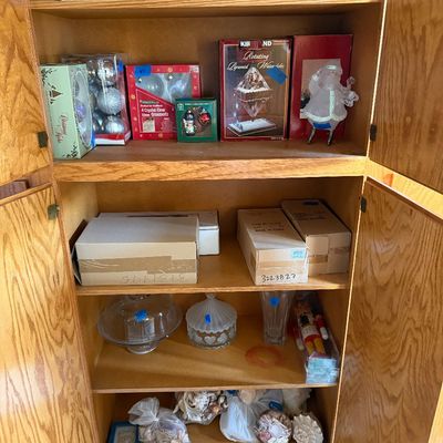 Sale Photo Thumbnail #104: Wooden cabinet filled with various household items, including packaged holiday ornaments, nativity scene, boxed goods, glassware, and a sea shell collection.